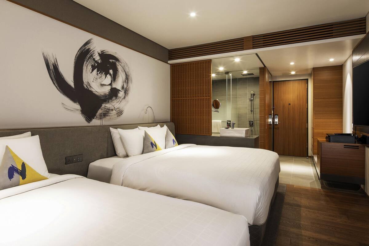 A hotel room with two beds, a large abstract painting, a modern bathroom, and wooden paneling.