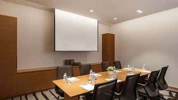 Un salón de conferencias con una larga mesa, sillas, una pantalla de proyector y un dispensador de agua.