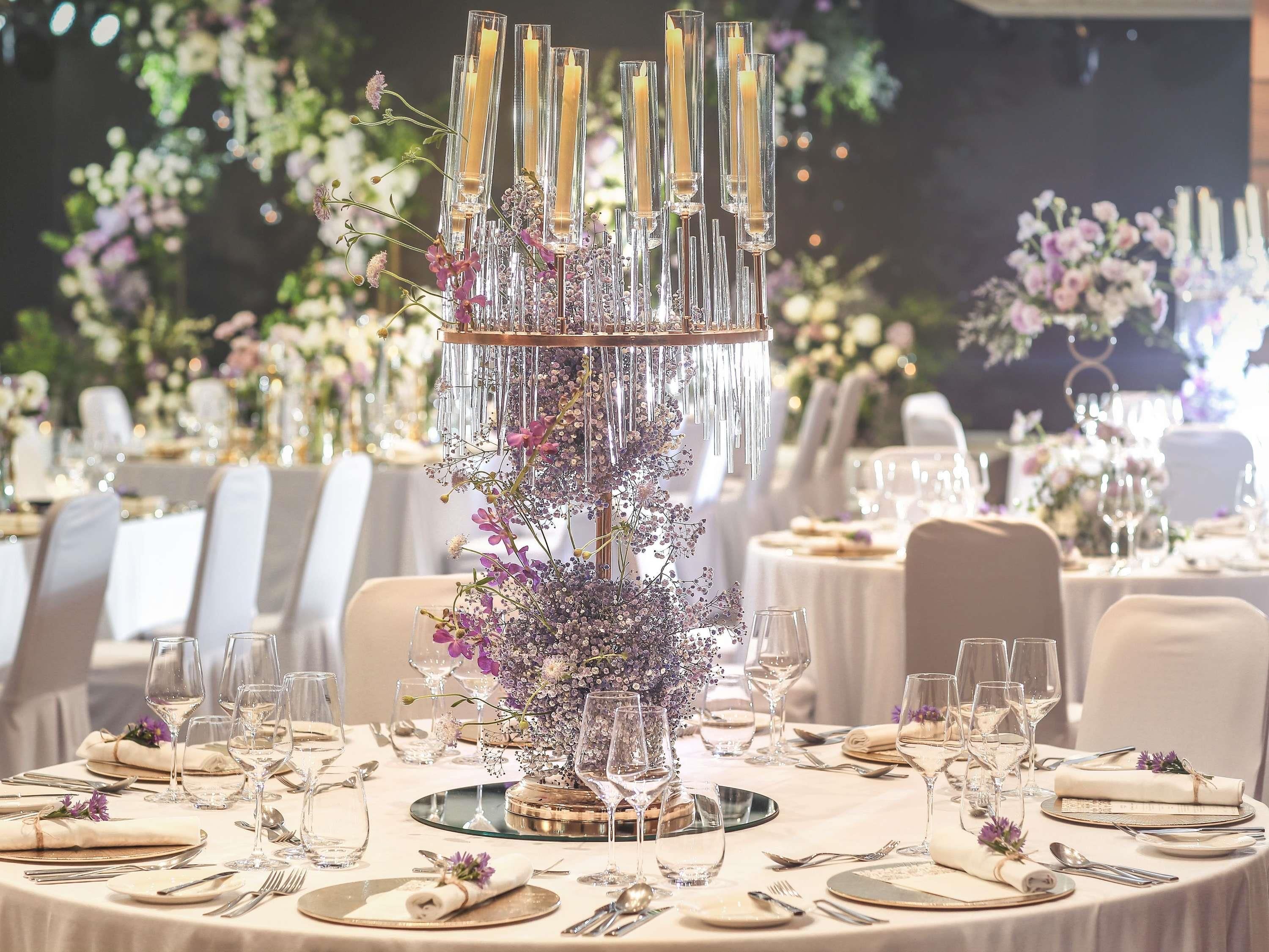 A round table with a central decorative piece, surrounded by chairs and set with fine dining ware.