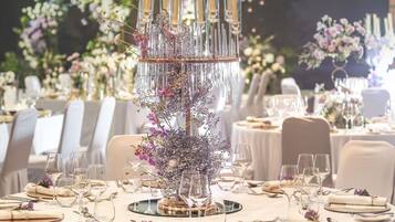 A round table with a central decorative piece, surrounded by chairs and set with fine dining ware.