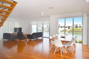 A spacious living room with a wooden floor, a dining table with chairs, a TV, and a staircase. - 4/84 The Anchorage, (Port Macquarie)
