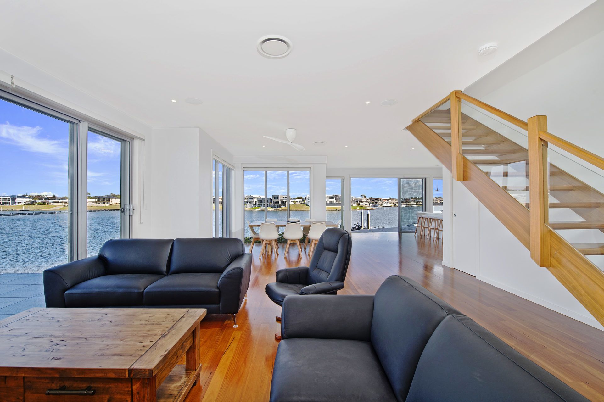 A spacious living area with a view of the water, a wooden staircase, and modern furniture.