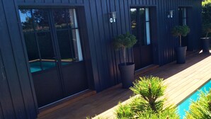 A modern building with large windows, a wooden deck, and a pool.