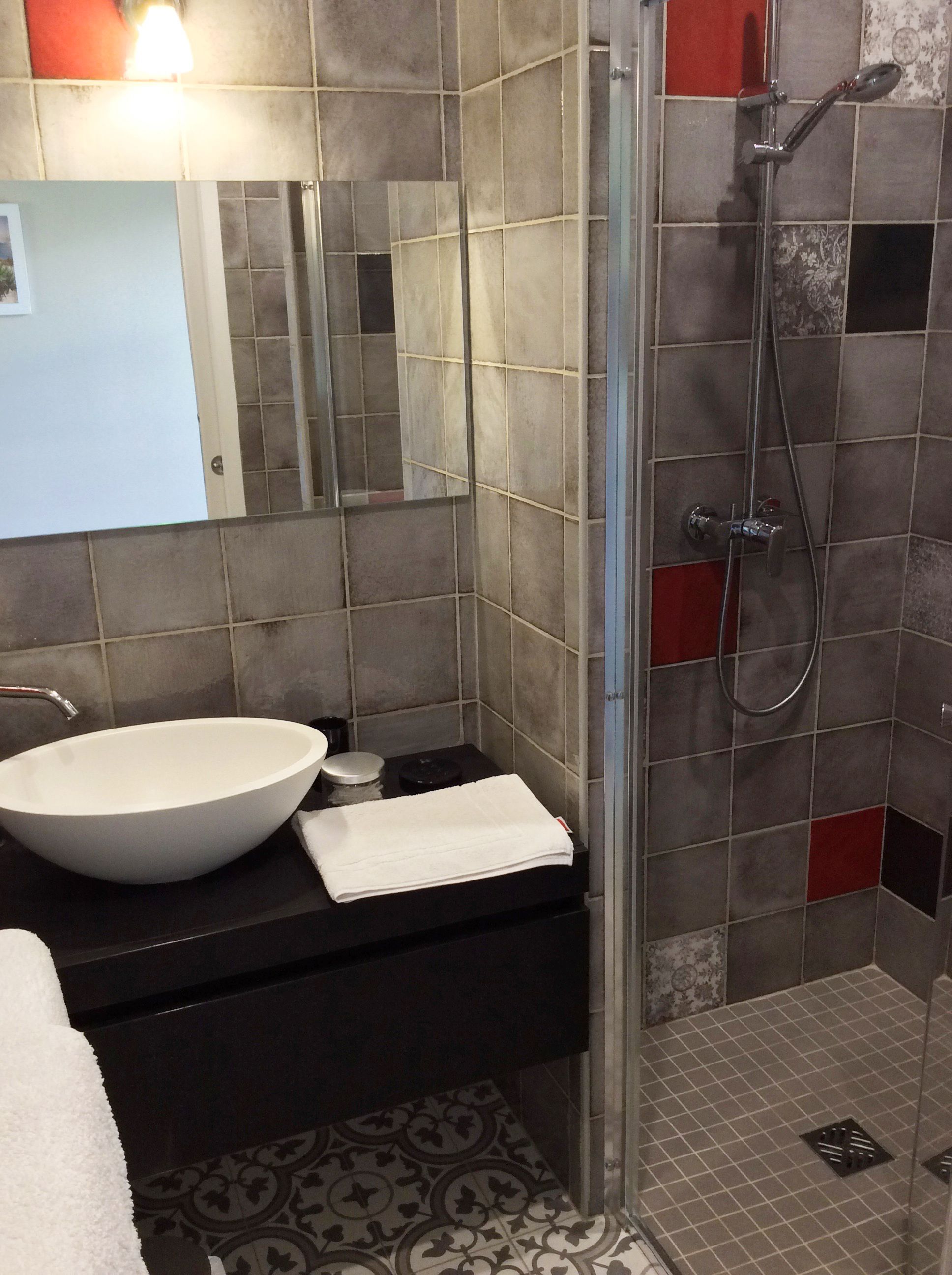A bathroom with a large white sink, a mirror, a towel, and a shower area with tiled walls and floor.