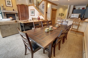 A dining area with a wooden table and chairs, a fireplace, and a kitchen in the background. - Ski Tip Ranch 8701 (Keystone)