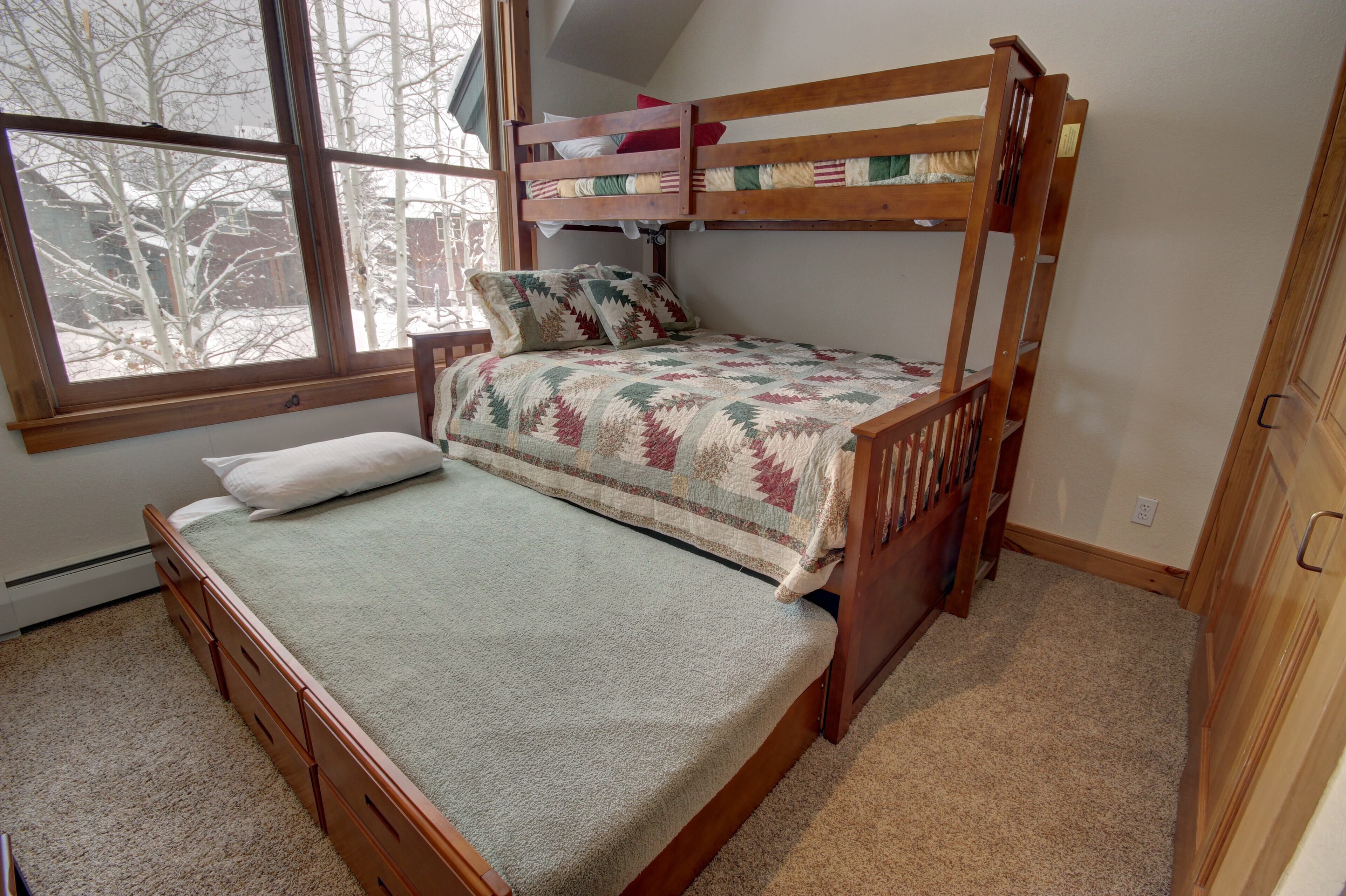 A bunk bed with a quilted bedspread, a window with a view of trees, and a carpeted floor.