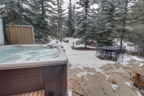 A hot tub, stone patio, wooden deck, and outdoor seating area surrounded by snow-covered trees. - Ski Tip Ranch 8701 (Keystone)