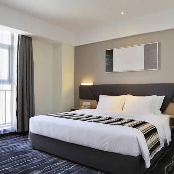 Ein Hotelzimmer mit einem großen Bett, einem dunklen Kopfteil und einem Fenster mit Vorhängen.