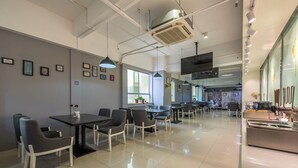 Un restaurant moderne au design épuré et minimaliste, offrant différents types de sièges et doté d’un grand écran de télévision.