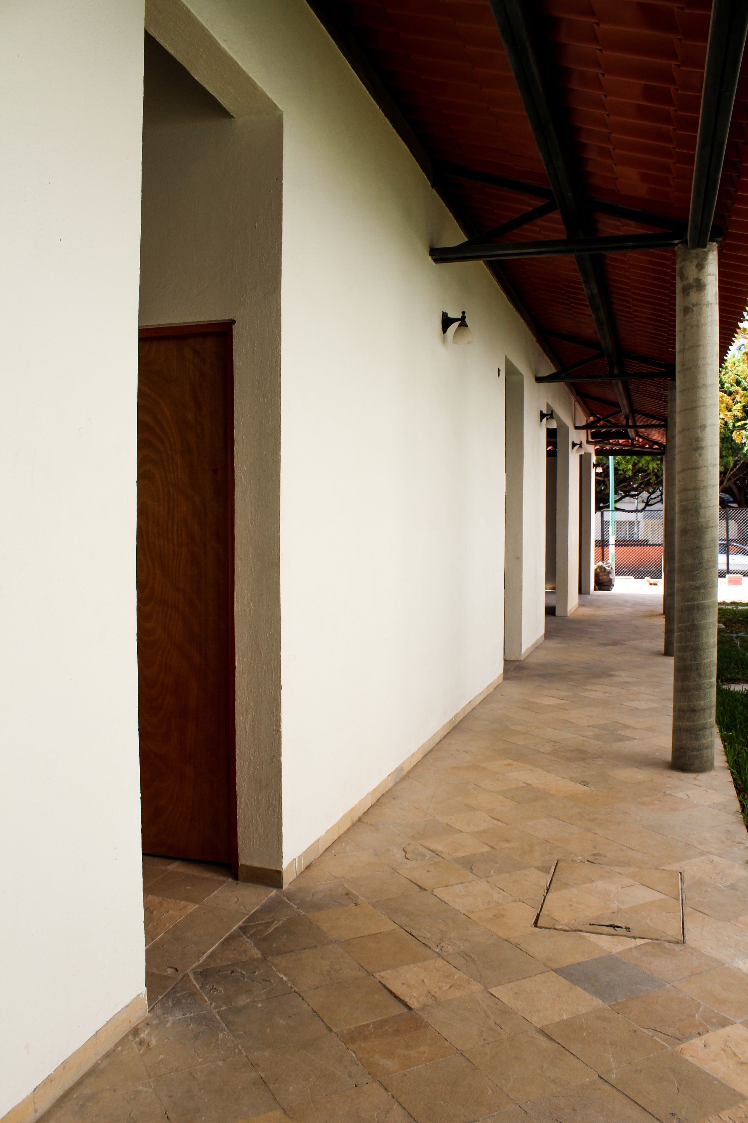 A covered corridor with tiled flooring, wooden doors, and a red roof structure.