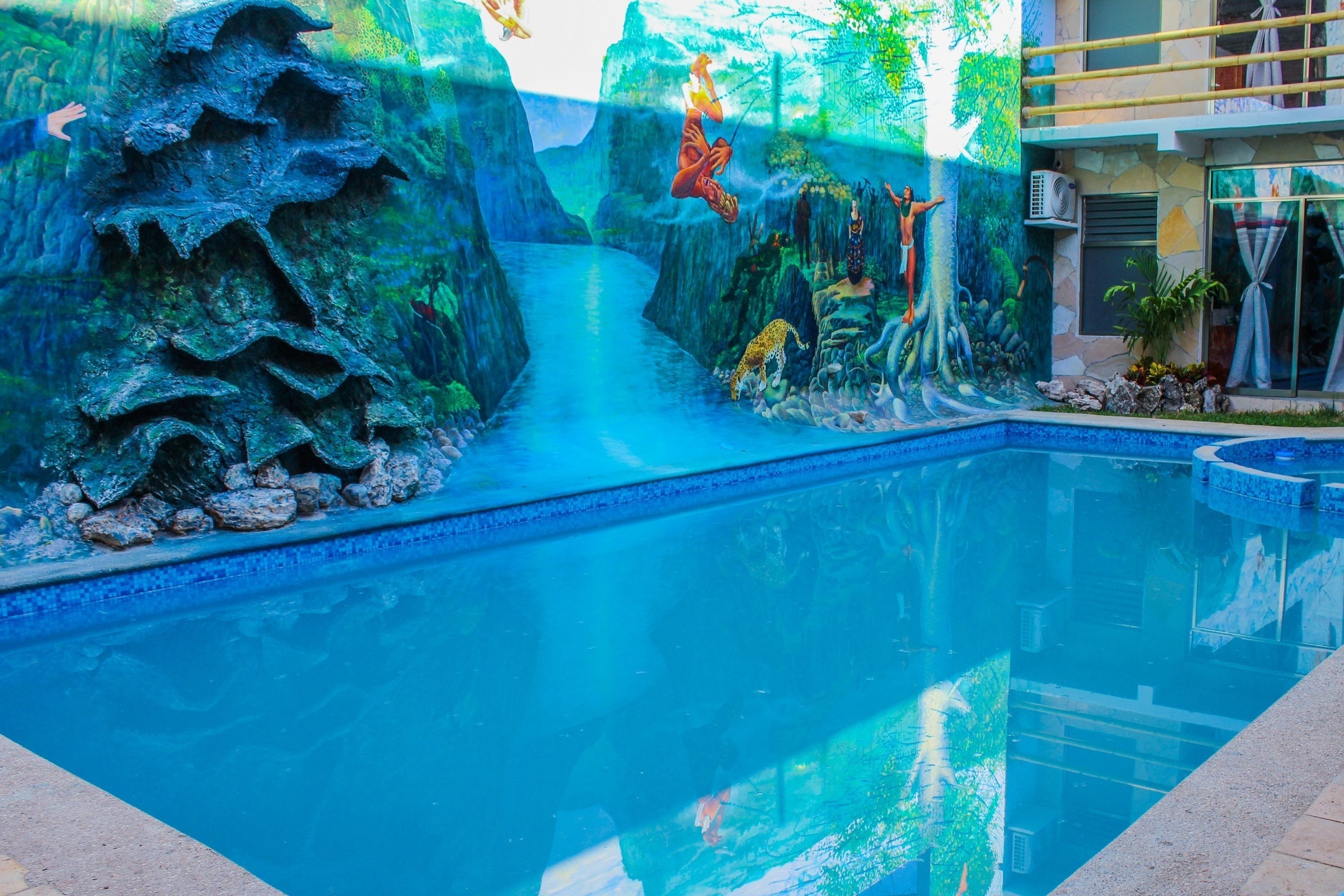 A swimming pool with a waterfall feature, surrounded by a rocky landscape and tropical vegetation.