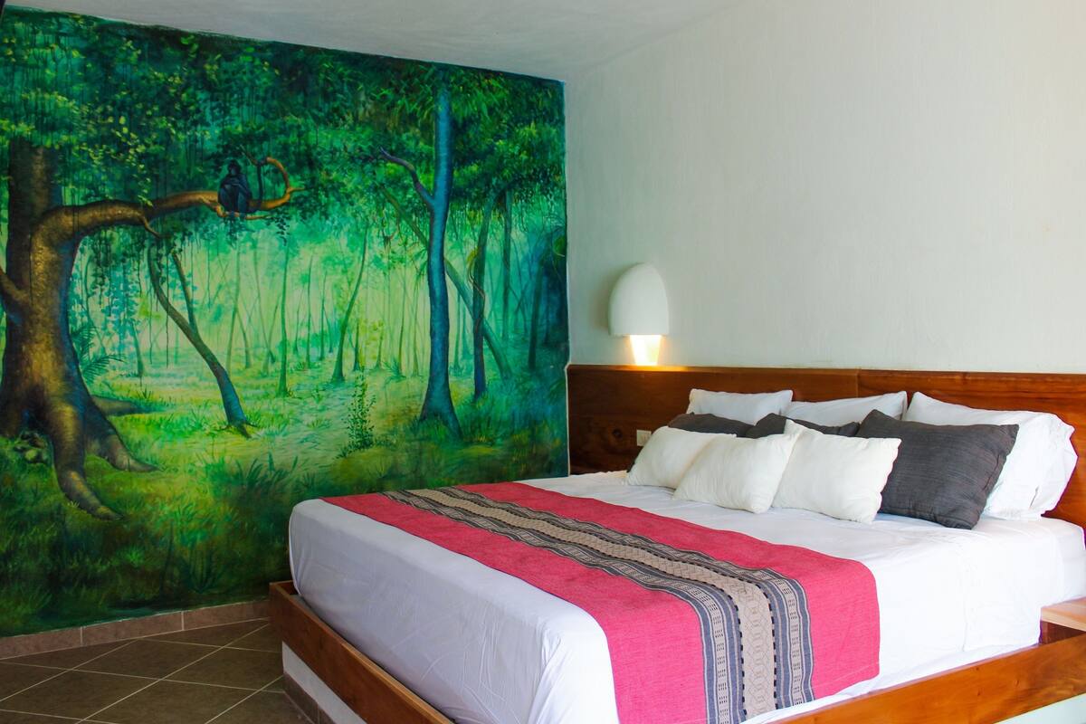 Et soveværelse med et stort mural af et skovmotiv, en træsenggavl og en sengebordlampe.