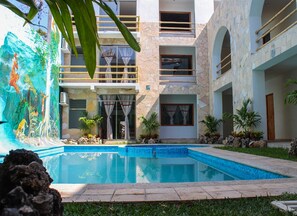 Um edifício moderno com piscina, fachada de pedra e um mural tropical.