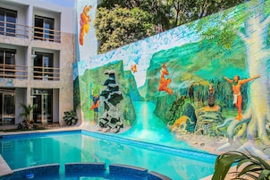 Una piscina con un mural que representa escenas de selva y un edificio con balcones.