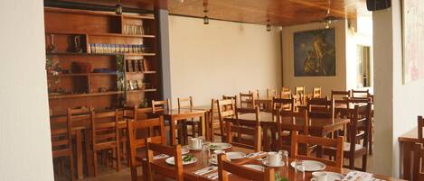 Un comedor con mesas y sillas de madera, un ventilador de techo y una estantería con diversos objetos.