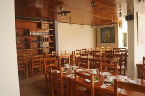A dining area with wooden tables and chairs, a ceiling fan, and a bookshelf with various items. - Axkan Arte Hotel Tuxtla (Tuxtla Gutierrez)
