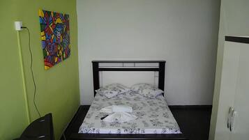 A single bed with a floral bedspread, a black headboard, and a colorful abstract painting on the wall.