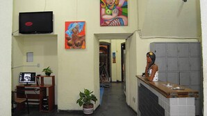 A reception area with a desk, a TV mounted on the wall, and two paintings. - Pousada Solar dos Romanos (Salvador)