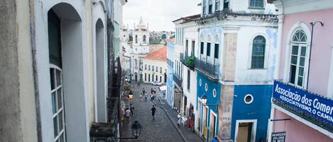 A narrow cobblestone street lined with colorful buildings, a white van parked on the side, and people walking.