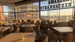 A modern restaurant with high tables and chairs, large windows offering city views, and a sign reading "RESTAURANT". - Hotel Express 53 (Bogotá)