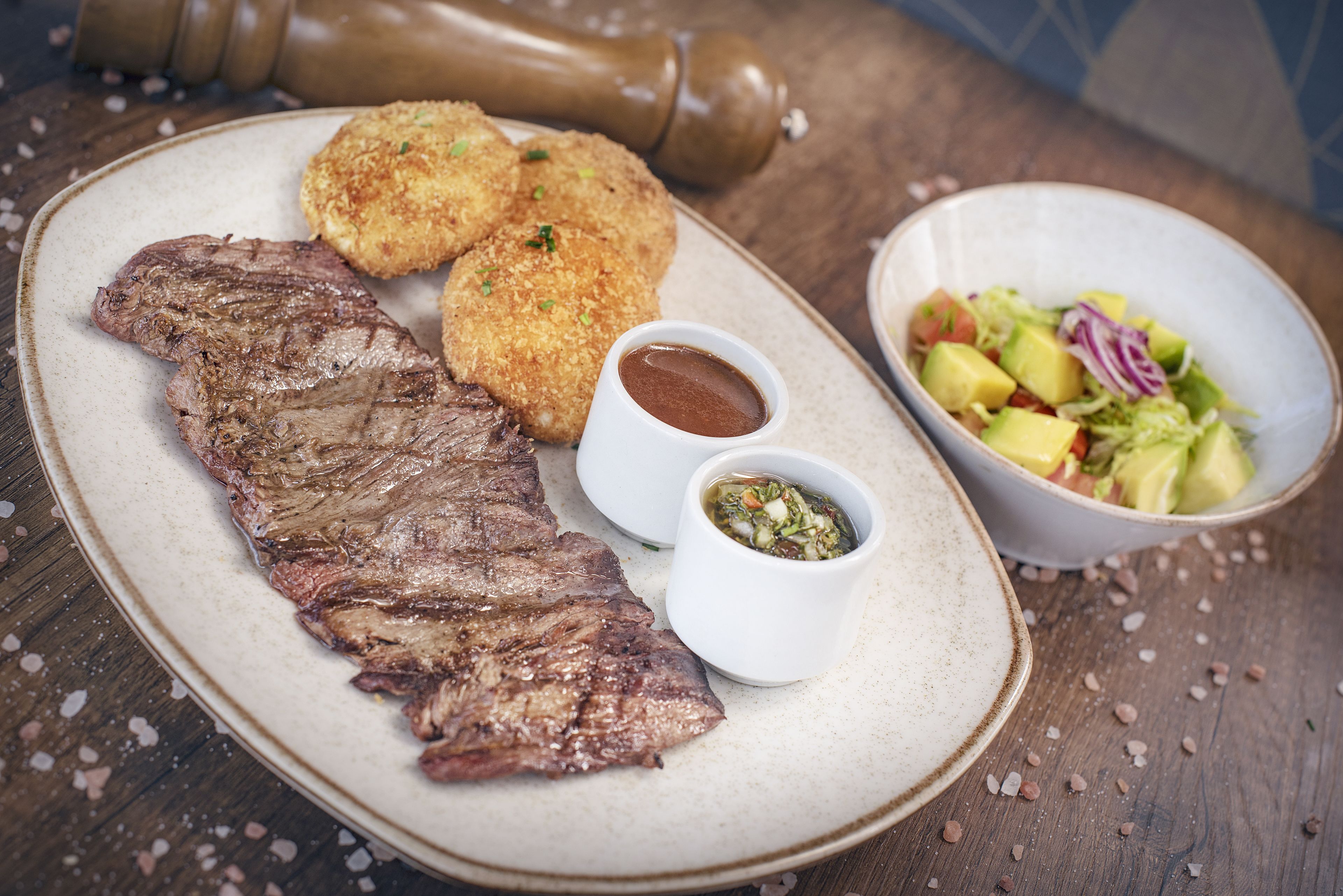 A plate with grilled steak, two breaded items, and a bowl of salad.