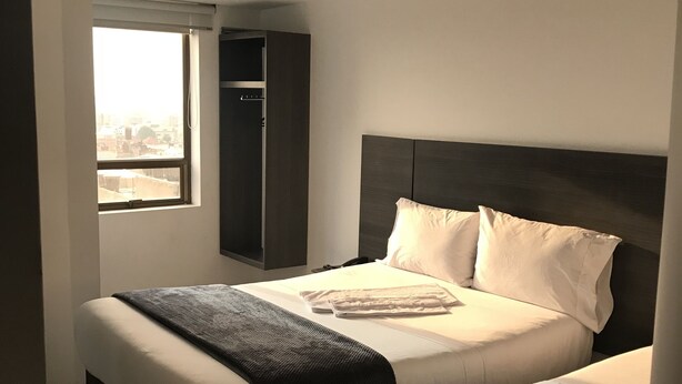 A hotel room with two beds, a wardrobe, and a window with a view. - Hotel Express 53 (Bogotá)