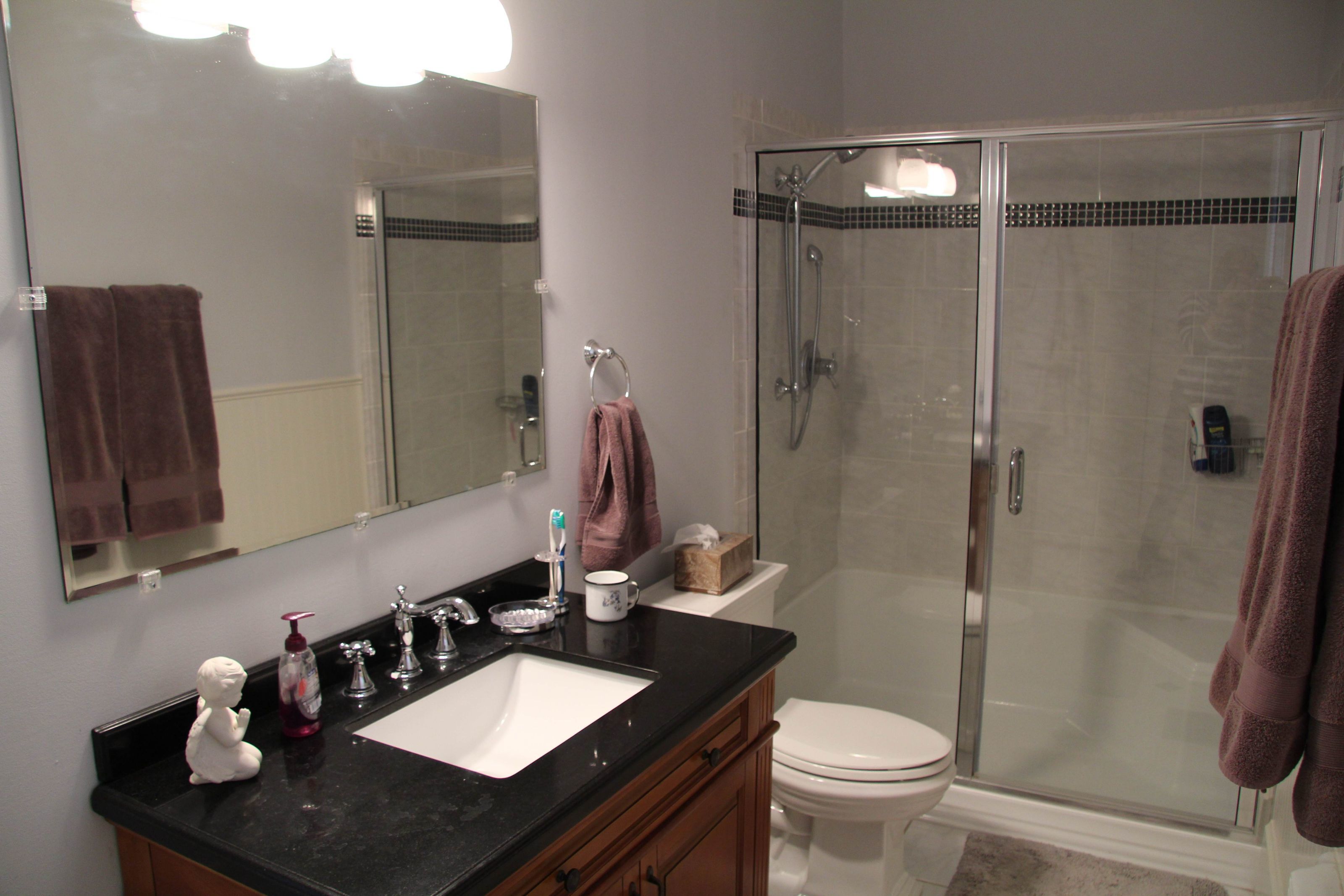A bathroom with a black countertop, a white sink, a glass-enclosed shower, and a white toilet.