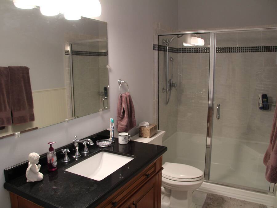 A bathroom with a black countertop, a white sink, a glass-enclosed shower, and a white toilet.