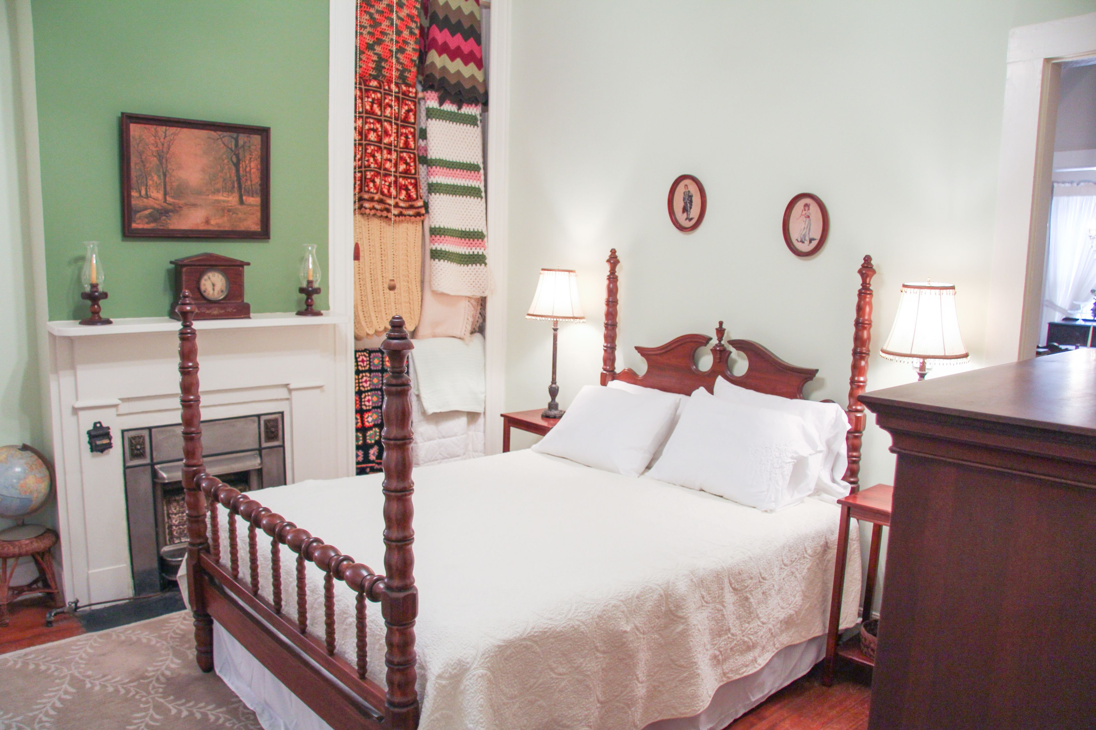A traditional bedroom with a four-poster bed, a fireplace, and two wall-mounted lamps.