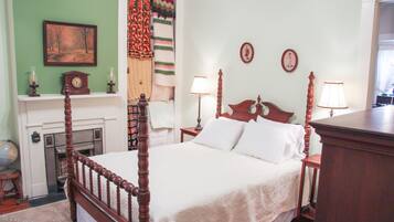 A traditional bedroom with a four-poster bed, a fireplace, and two wall-mounted lamps.