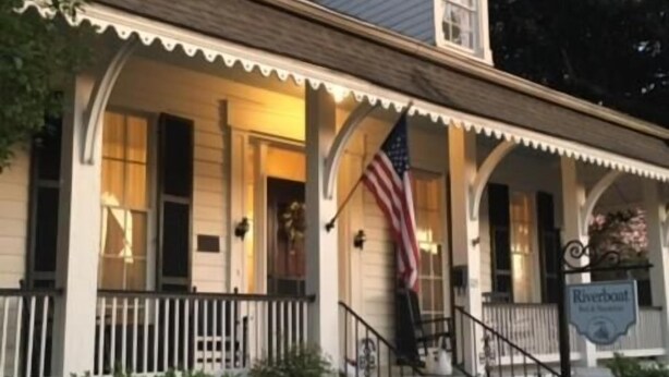 A two-story house with a porch, a white picket fence, and an American flag. - Riverboat Bed & Breakfast (Natchez)