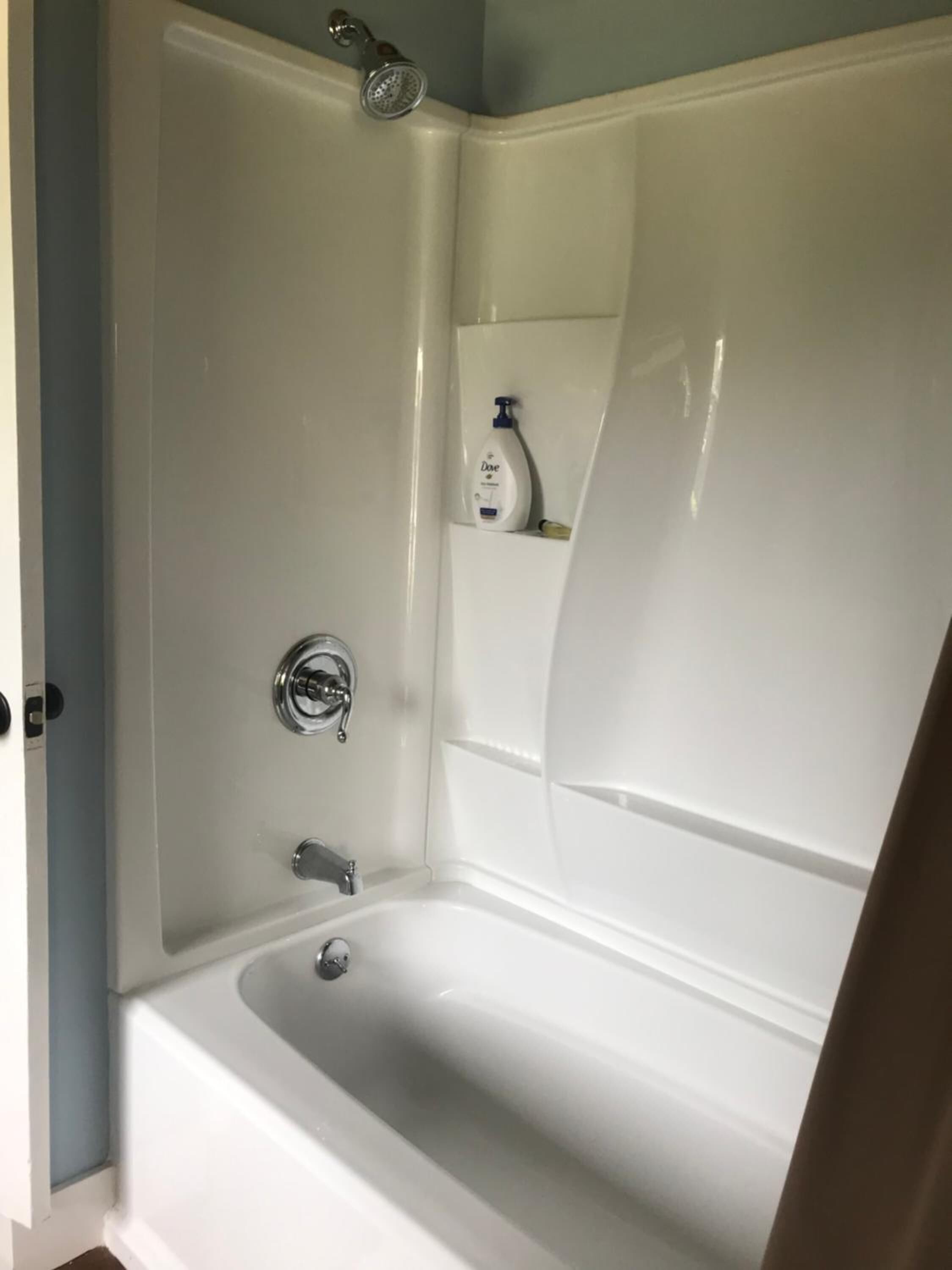 A bathroom with a white bathtub, a showerhead, and a bottle of Dove soap on a shelf.
