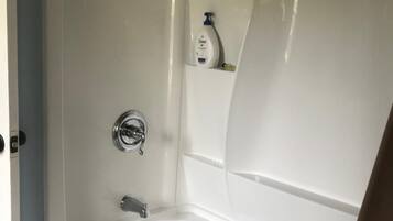 A bathroom with a white bathtub, a showerhead, and a bottle of Dove soap on a shelf.