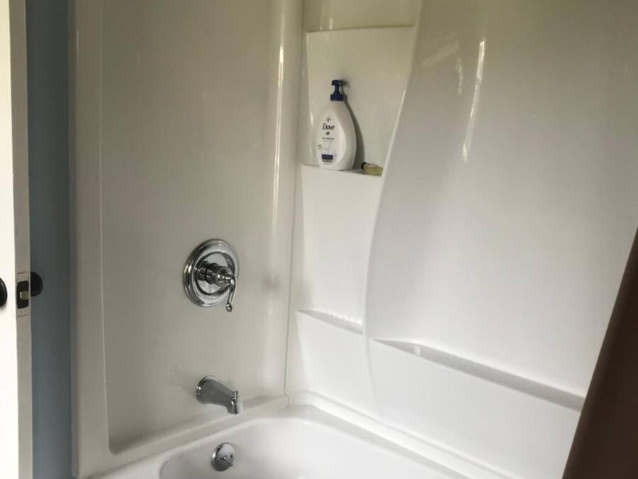 A bathroom with a white bathtub, a showerhead, and a bottle of Dove soap on a shelf.