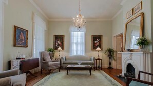 A traditional living room with a sofa, armchairs, a coffee table, a fireplace, and decorative items. - Riverboat Bed & Breakfast (Natchez)
