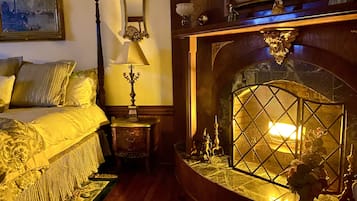 A traditional room with a bed, a mirror, a lamp, and a fireplace with decorative items.
