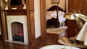 A spacious room with a large bathtub, a fireplace, and a bed with a wooden headboard. - Hogan House at Rose Hill B&B (Hogansville)