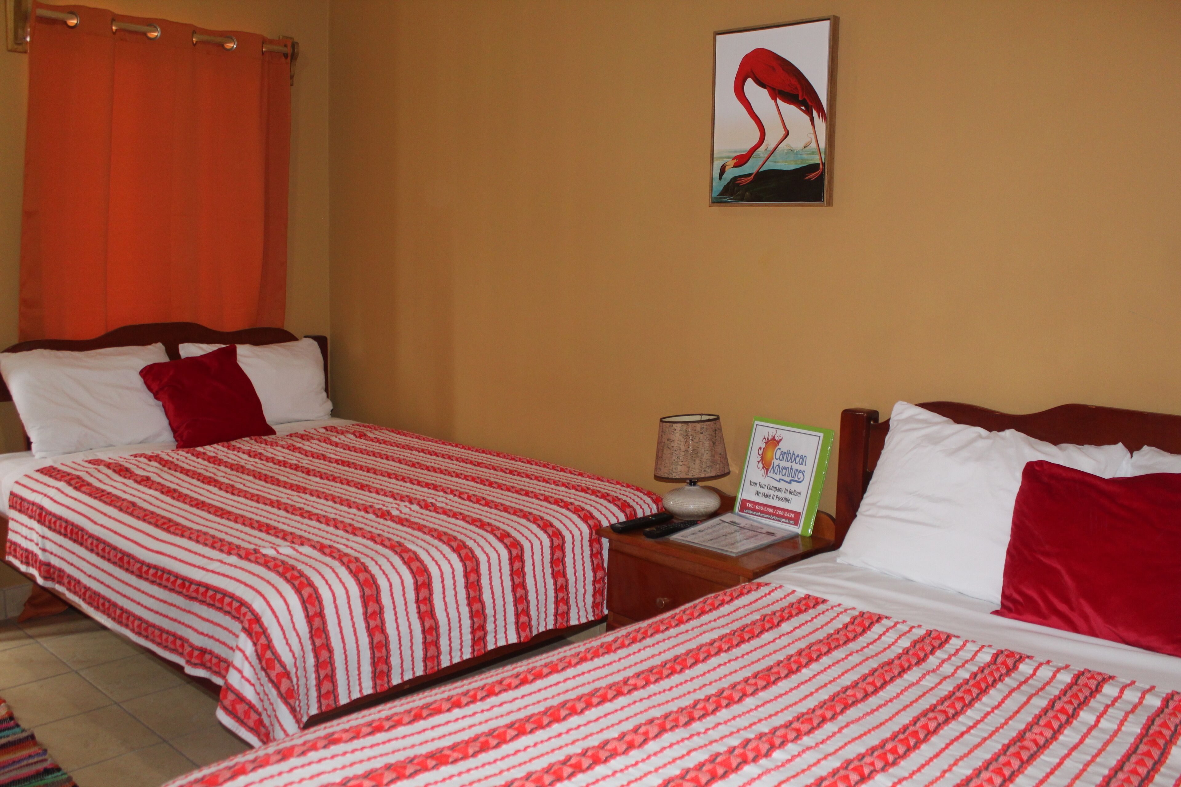 A hotel room with two beds, each with red and white striped bedding, a nightstand with a lamp, and a painting of a flamingo on the wall.
