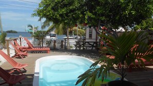 A pool area with a wooden deck, red lounge chairs, and a palm tree. - Ambergris Sunset Hotel (San Pedro)
