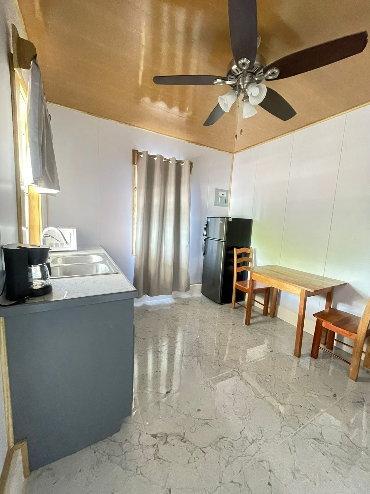 Una cocina compacta con refrigerador, cafetera y ventilador de techo.
