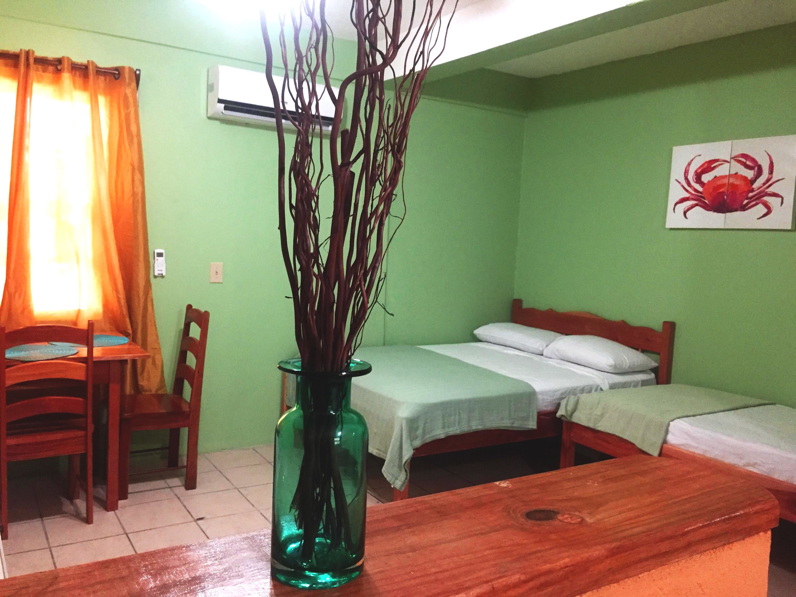A room with a bed, a chair, a table, and a vase with branches.