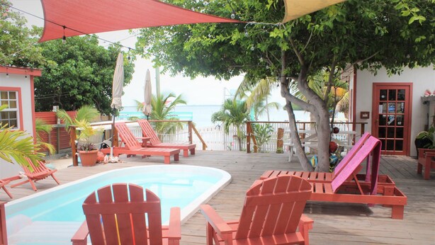 A wooden deck with a pool, red Adirondack chairs, and a view of the ocean. - Ambergris Sunset Hotel (San Pedro)