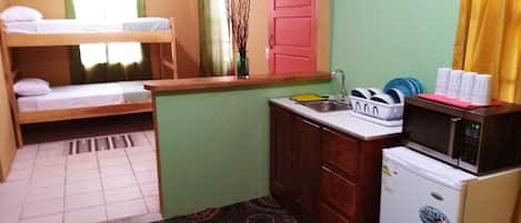A small, compact room with bunk beds, a kitchenette, and a patterned rug.