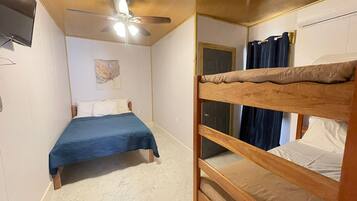 A room with a bunk bed, a single bed, a ceiling fan, a door, and a wall-mounted TV.