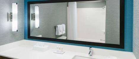 A modern bathroom with a large mirror, white sink, and a towel rack.