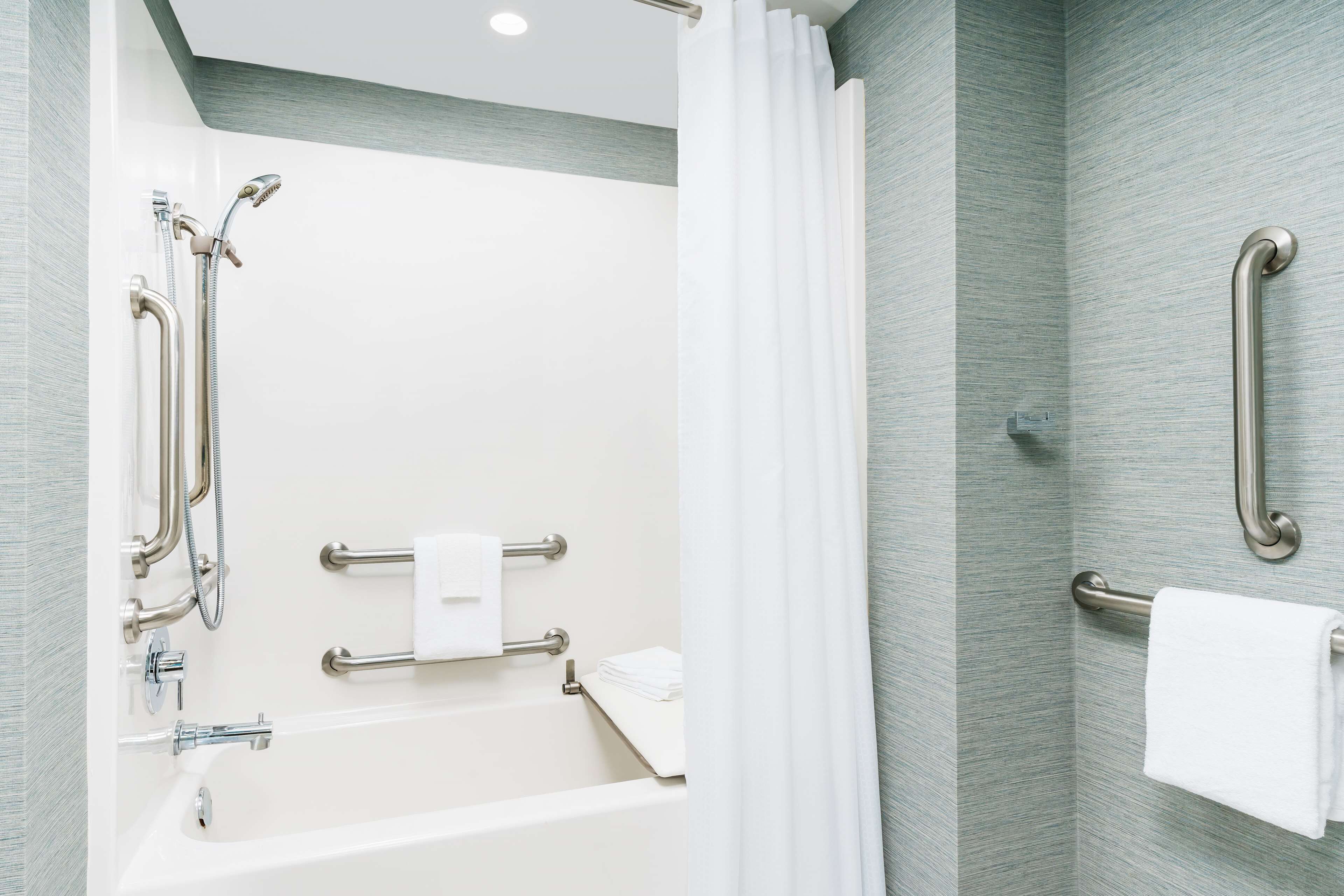 Une salle de bain moderne équipée d’une baignoire, de barres d’appui et d’une douche avec un pommeau de douche amovible.