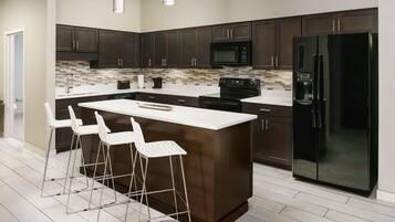 A modern kitchen with dark wood cabinets, a large island with bar stools, a black refrigerator, and a microwave.