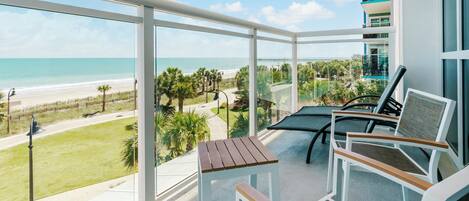 A balcony with a view of the beach, a table, and two chairs.