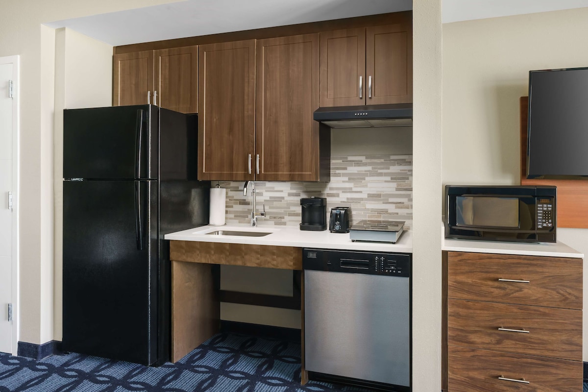 A compact kitchen with wooden cabinets, a black refrigerator, a microwave, and a dishwasher.