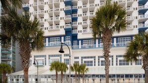 A multi-story hotel with balconies, palm trees, and a glass conservatory.